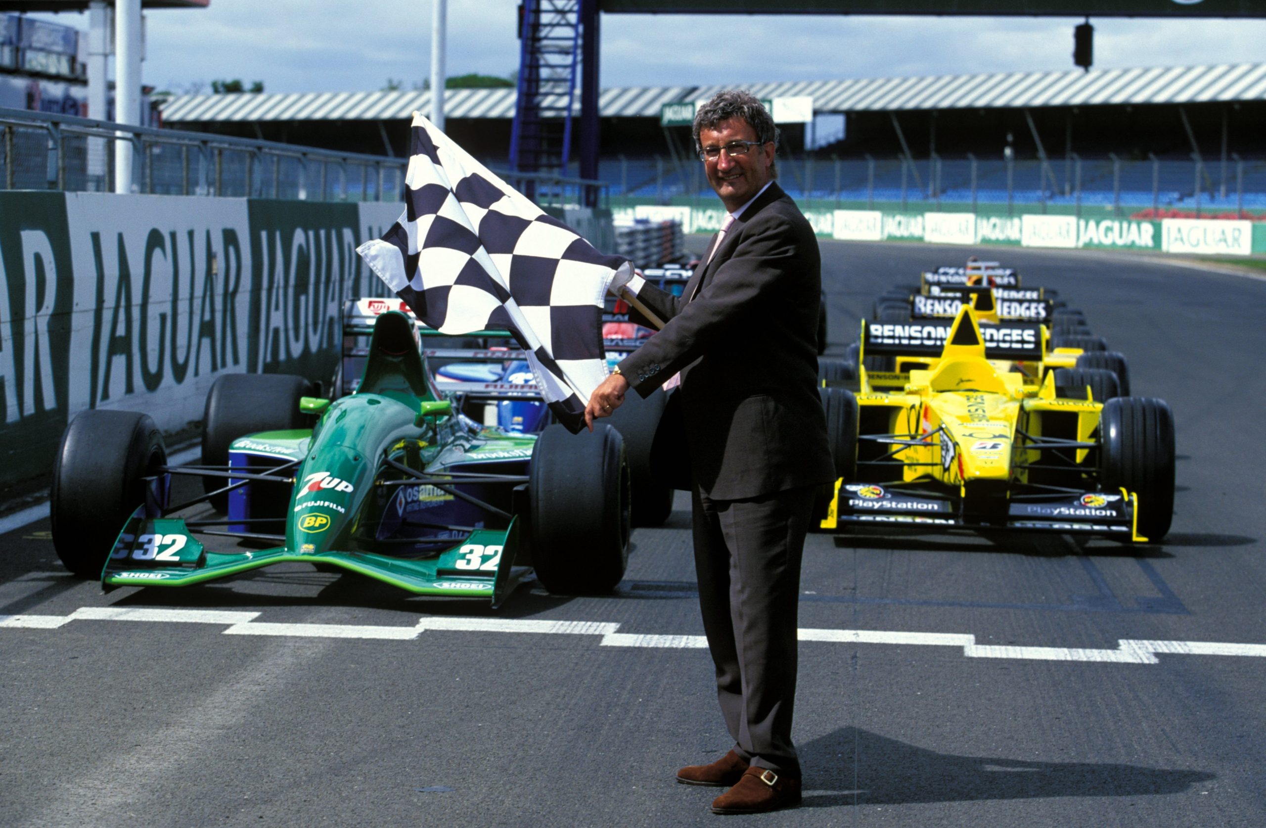 L'ancien chef d'équipe, Eddie Jordan, s'en est allé à 76 ans Eddie Jordan est décédé. Il tient un drapeau à damier devant deux monoplaces de F1